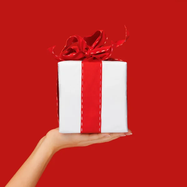 Close up hand holding christmas gift box over red — Zdjęcie stockowe