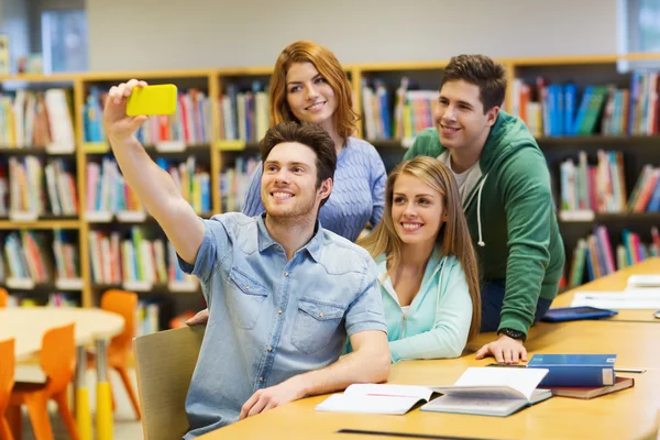 Estudantes com smartphone tirando selfie na biblioteca — Fotografia de Stock