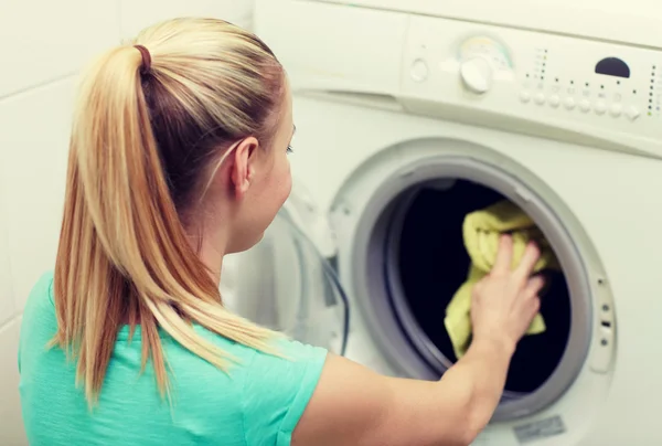 Mujer feliz poniendo la ropa en la lavadora en casa —  Fotos de Stock