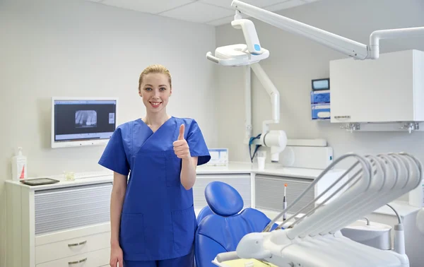 Dentista mujer feliz mostrando pulgares hacia arriba en la clínica —  Fotos de Stock