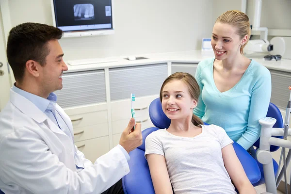 Dentista feliz mostrando escova de dentes para menina paciente — Fotografia de Stock