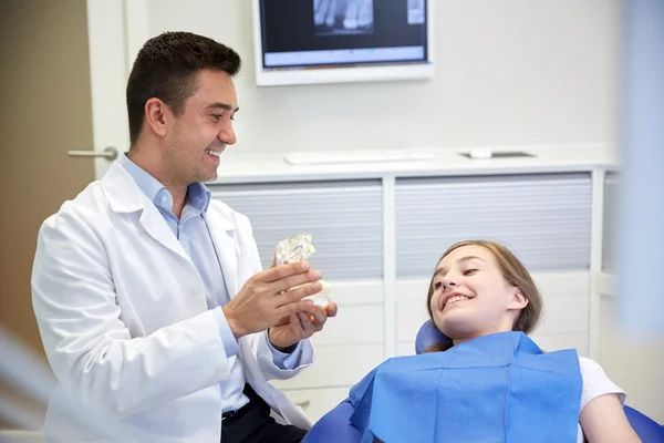 Щасливий стоматолог, що показує макет щелепи для пацієнтки — стокове фото