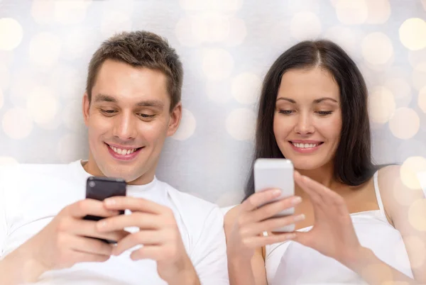 Lachende paar in bed met smartphones — Stockfoto