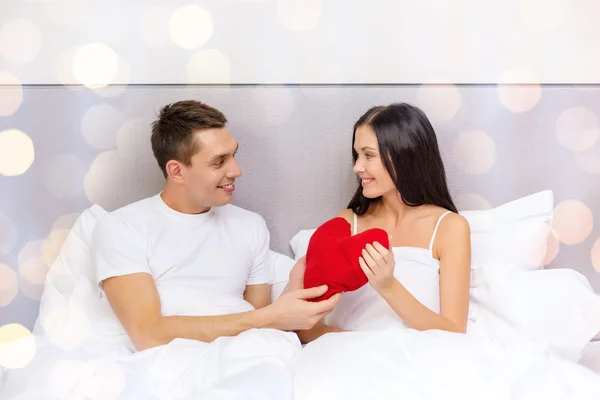 Couple souriant au lit avec oreiller en forme de coeur rouge — Photo