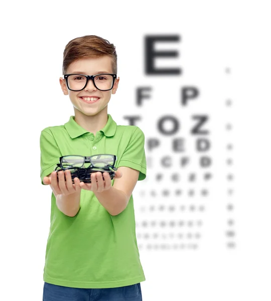 Happy boy holding eyeglasses over eye chart — Stockfoto