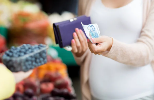 Pregnant woman with wallet buying beries at market — Stock fotografie