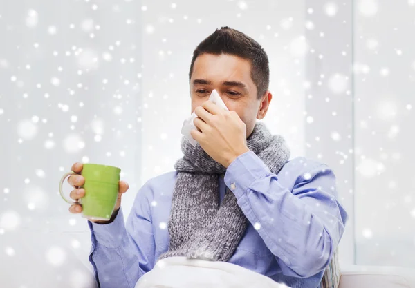 Zieke man met griep drinken thee en blazen neus — Stockfoto