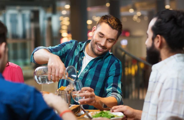 Happy man with friends pouring water at restaurant — Stock Photo, Image