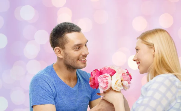 Smiling man giving woman flowers at home — ストック写真