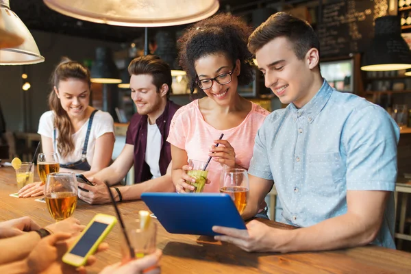 Happy friends with tablet pc and drinks at bar — Stock Photo, Image