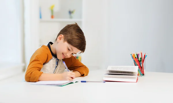 Lächelnder Studentenjunge schreibt zu Hause an Notizbuch — Stockfoto