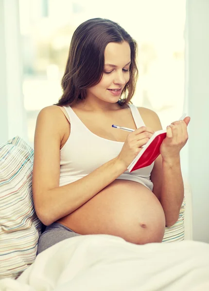 Ευτυχισμένος έγκυος γυναίκα εγγράφως στο σημειωματάριο στο σπίτι — Φωτογραφία Αρχείου