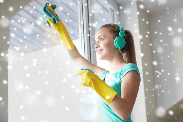 Happy woman with headphones cleaning window — Stock Photo, Image