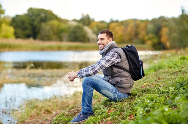 在河岸边休息，背包里的男人微笑着 — 图库照片