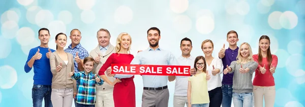 Happy people with red sale sign showing thumbs up — Stock Photo, Image