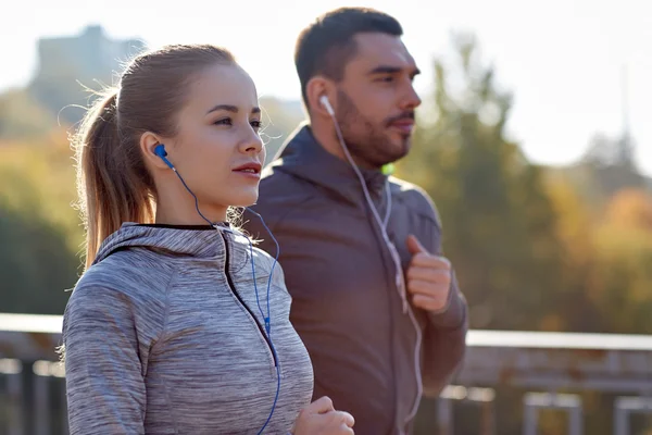 Feliz pareja con auriculares funcionando en la ciudad — Foto de Stock