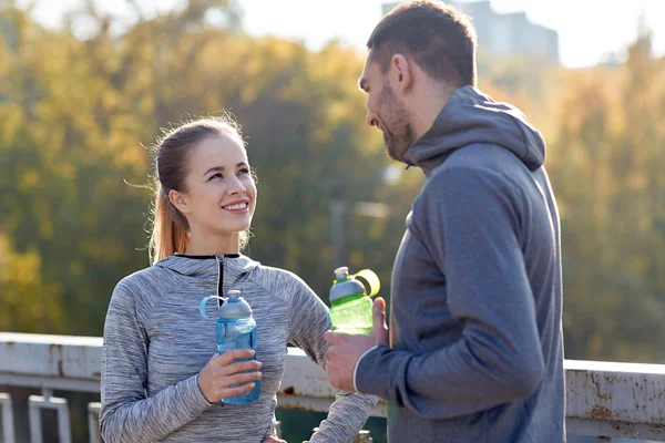 Улыбающаяся пара с бутылками воды на открытом воздухе — стоковое фото