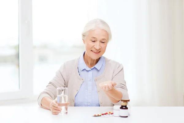 Happy senior woman with water and medicine at home — Stock Photo, Image