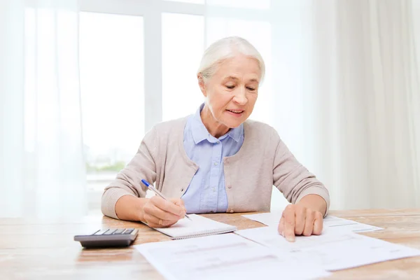 Пожилая женщина с бумагами и калькулятором дома — стоковое фото