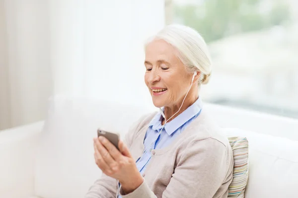 Senior vrouw met smartphone en oortelefoons thuis — Stockfoto