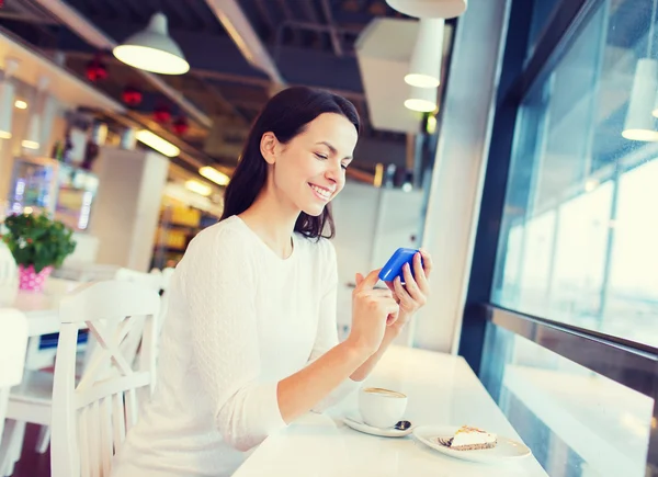 Улыбающаяся женщина со смартфоном и кофе в кафе — стоковое фото