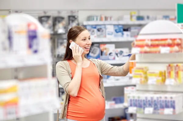 Mujer embarazada feliz con teléfono inteligente en la farmacia —  Fotos de Stock