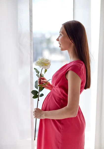 Glad gravid kvinna med rosa blomma hemma — Stockfoto