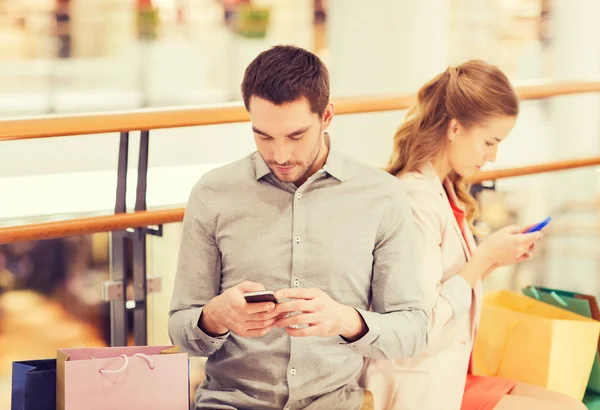 Pareja con smartphones y bolsas de compras en el centro comercial — Foto de Stock