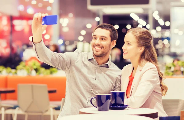 Happy couple with smartphone taking selfie in mall — Stock Photo, Image