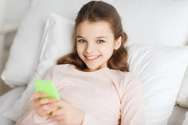 Menina feliz deitado na cama com smartphone em casa — Fotografia de Stock