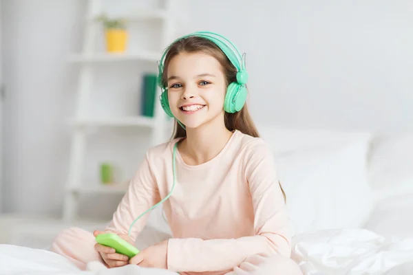 Mädchen sitzt mit Smartphone und Kopfhörer im Bett — Stockfoto