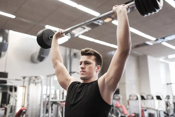 Young man flexing muscles with barbell in gym — Stock Photo, Image