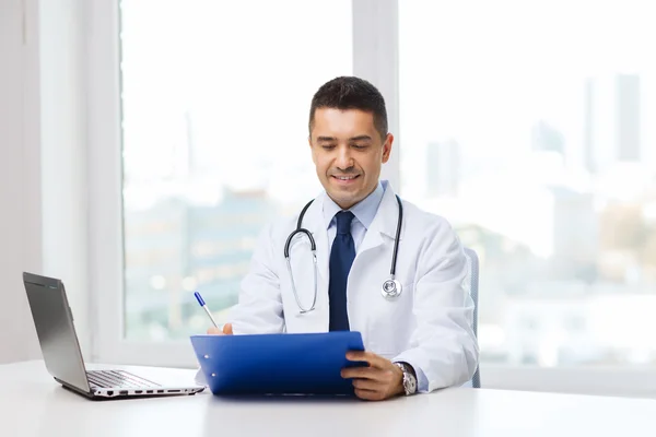 Zufriedener Arzt mit Klemmbrett und Laptop im Büro — Stockfoto
