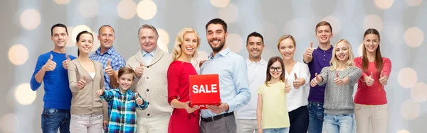 Happy people with red sale sign showing thumbs up — Stock Photo, Image