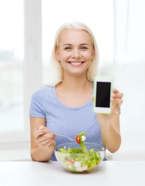 Mujer sonriente con smartphone comiendo ensalada en casa — Foto de Stock