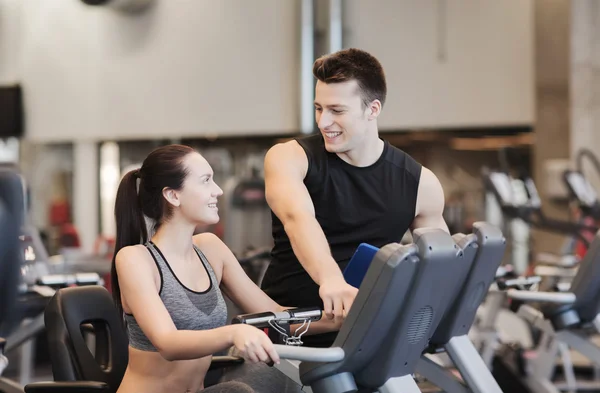 Glad kvinna med tränare på motionscykel i gym — Stockfoto