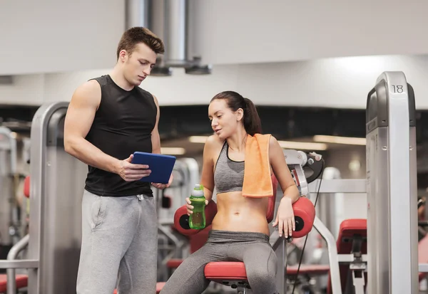 Giovane donna sorridente con personal trainer in palestra — Foto Stock