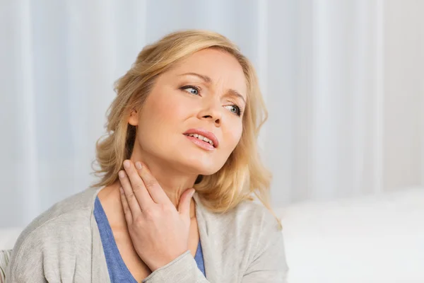 Unhappy woman suffering from throat pain at home Stockbild