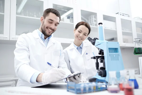 Wetenschappers met Klembord en Microscoop in lab — Stockfoto