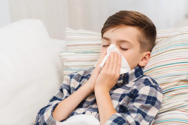 Zieke jongen in bed liggen en blazen zijn neus thuis — Stockfoto