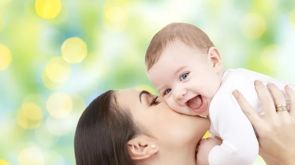 Mãe feliz beijando seu bebê sobre luzes verdes — Fotografia de Stock