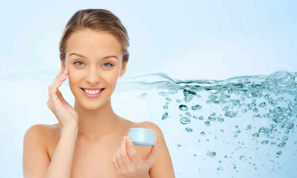 Sorrindo jovem mulher aplicando creme em seu rosto — Fotografia de Stock