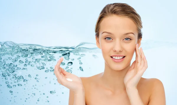 Smiling young woman applying cream to her face — Stok fotoğraf