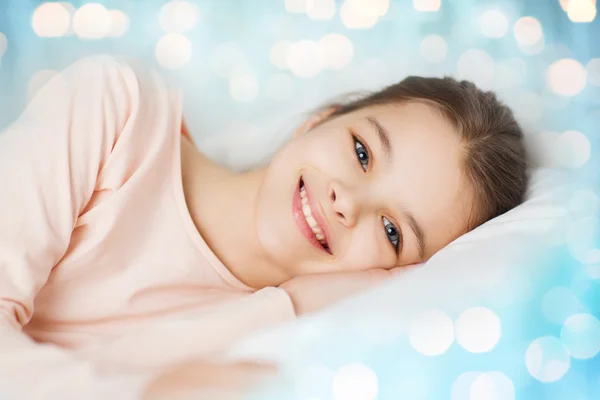 Happy smiling girl lying awake in bed over lights — Stock Photo, Image