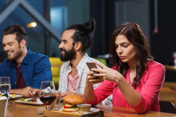 Mulher com smartphone e amigos no restaurante — Fotografia de Stock