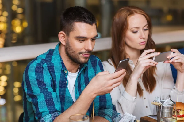 Paar mit Smartphones beim Essen im Restaurant — Stockfoto
