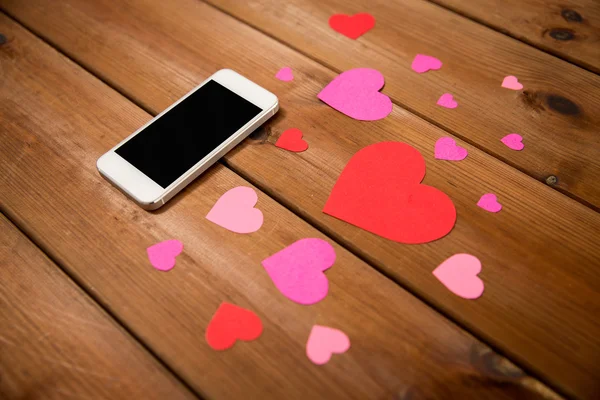 Close up of smartphone and hearts on wood — Stock Photo, Image