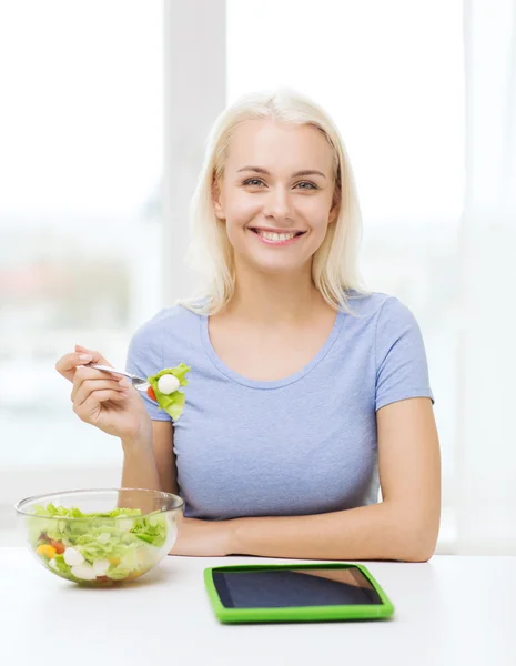 Lachende vrouw eten Salade met tablet pc thuis — Stockfoto