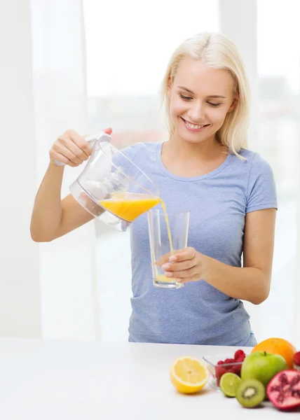 Mulher sorrindo derramando suco de frutas em vidro em casa — Fotografia de Stock