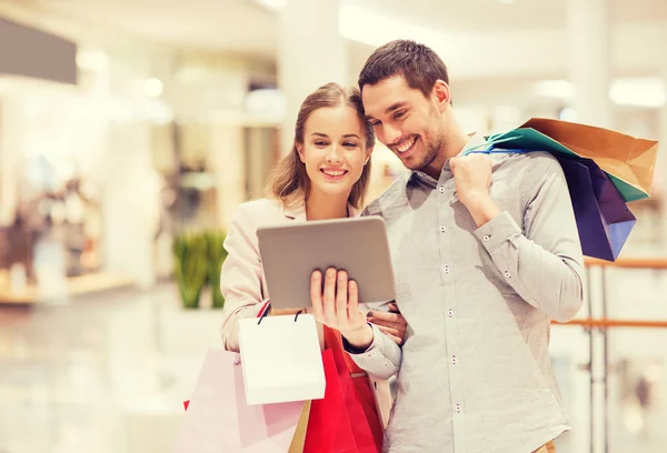 Pareja con tablet pc y bolsas de compras en el centro comercial —  Fotos de Stock